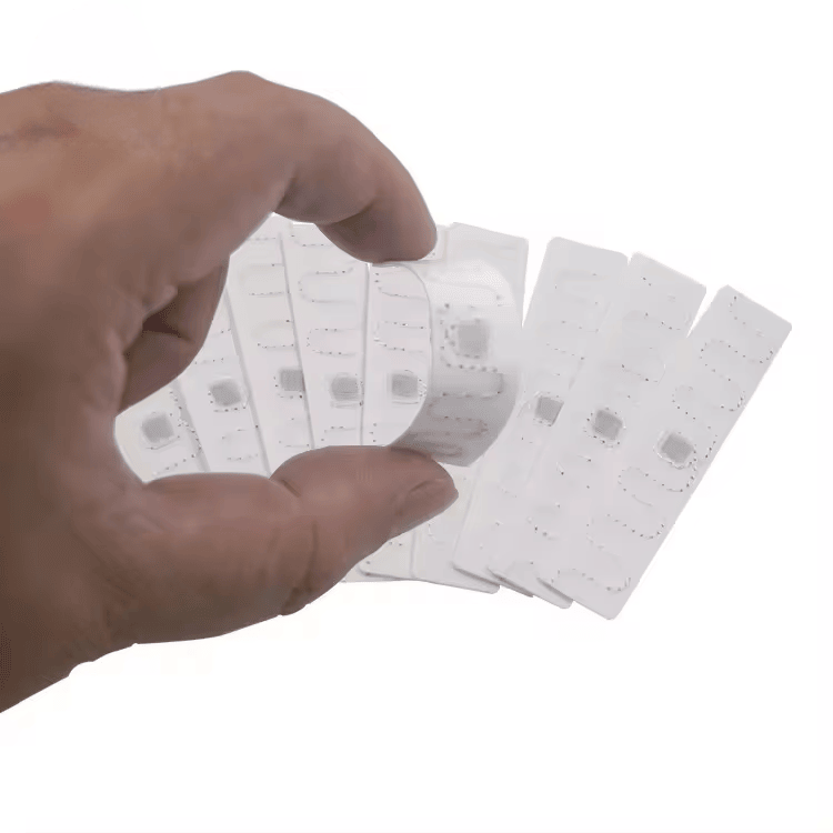 O mână ține mai multe RFID etichete de rufe T7015-2 din poliester pentru a demonstra senzația moale; flexibilă și forma ușoară pentru introducerea articolelor de îmbrăcăminte.