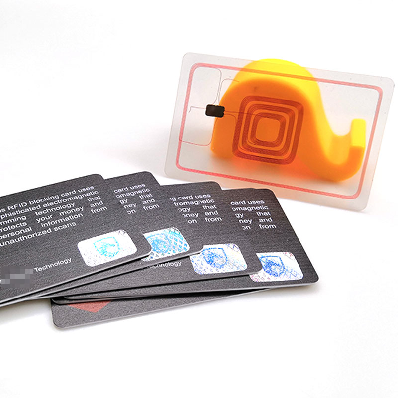 Ștergeți RFID incrustație care arată bobina antenei și cip plasat lângă un teanc de carduri de blocare RFID pentru a evidenția structura internă și ecranarea.