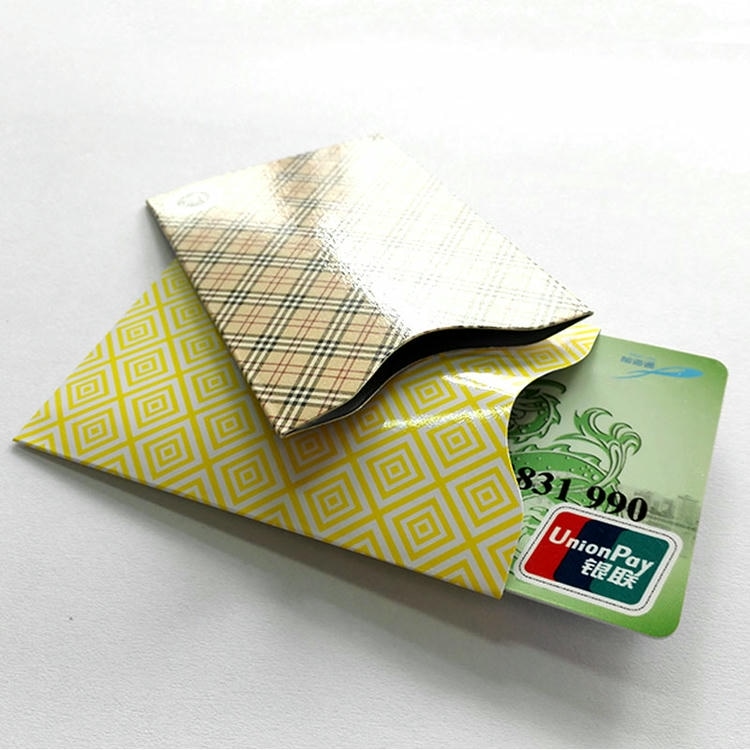 Card de plată extras parțial dintr-un manșon galben cu model RFID sub un manșon în carouri pentru a arăta o protecție practică în utilizare.