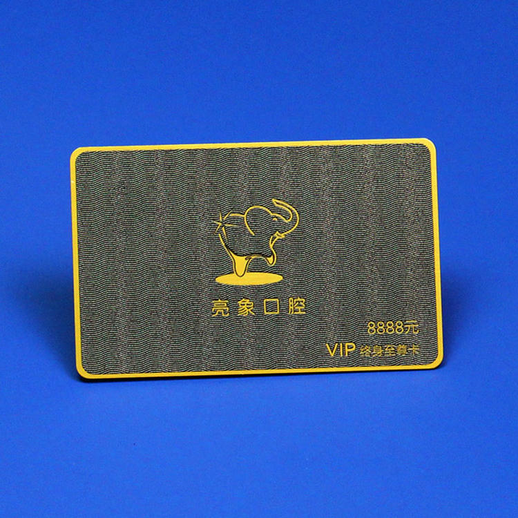 Card VIP din plastic negru texturat cu logo din folie aurie și margini aurii, prezentat pe fundal albastru de studio.