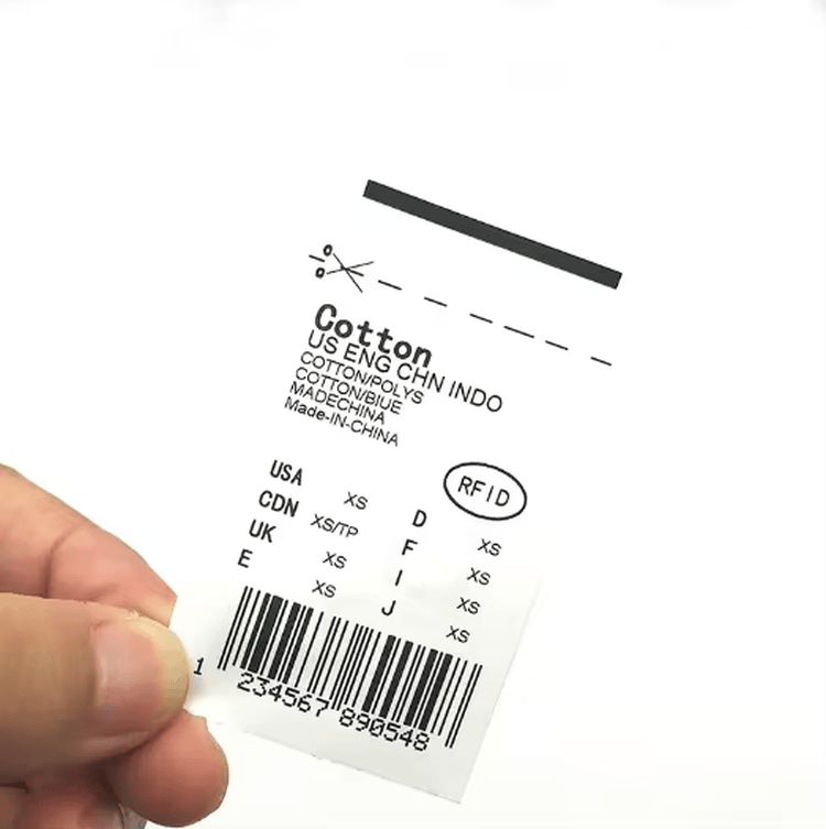 O mână ține o etichetă de îmbrăcăminte textilă transparentă RFID imprimată cu date despre dimensiunea bumbacului și informații despre codurile de bare pentru utilizarea îmbrăcămintei cusute.