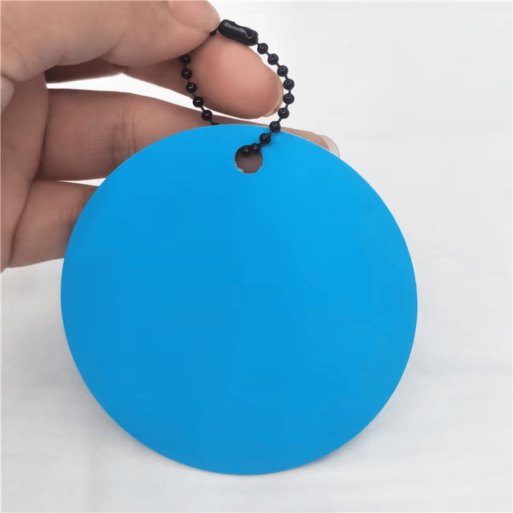 Vedere apropiată a unei etichete NFC rotunde albastre, cu lanț negru cu bile și orificiu de prindere poziționat aproape de margine.
