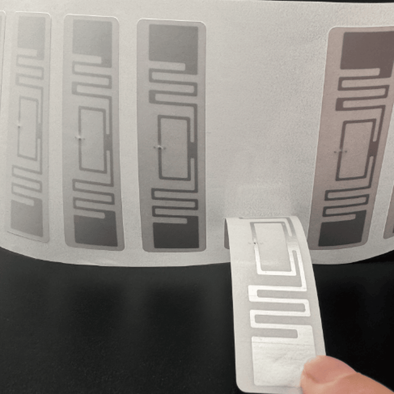 Imaginea de dezlipire arată etichete RFID UHF de 70x15mm alimentate din rolă pentru urmărirea cutiilor prin procese print-and-apply.