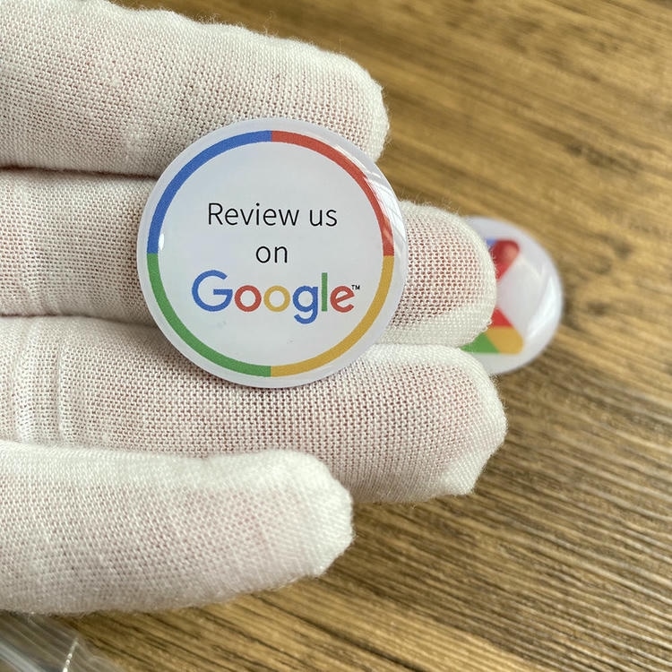 Autocolant epoxidic NFC cu formă personalizată; ținut cu o mână înmănușată; care arată o insignă de recenzie albă Google care acceptă acțiunile de atingere fără contact.